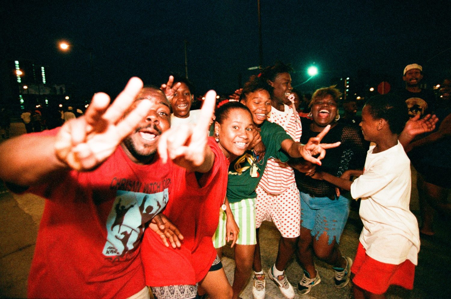 Color photograph of fans celebrating in the street. The closest fan to the camera is a Black man in a red t-shirt holding up three fingers to celebrate the three-peat.