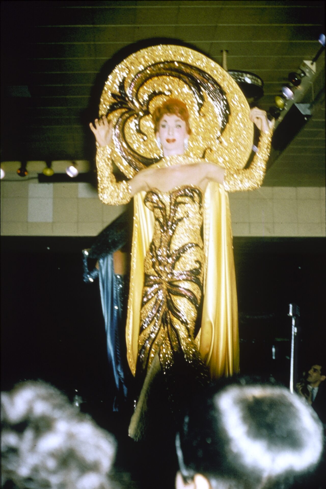 Jewel Box Revue drag show at Robert's Show Lounge. Female impersonator in yellow and black gown with a large yellow and black hat, on stage.