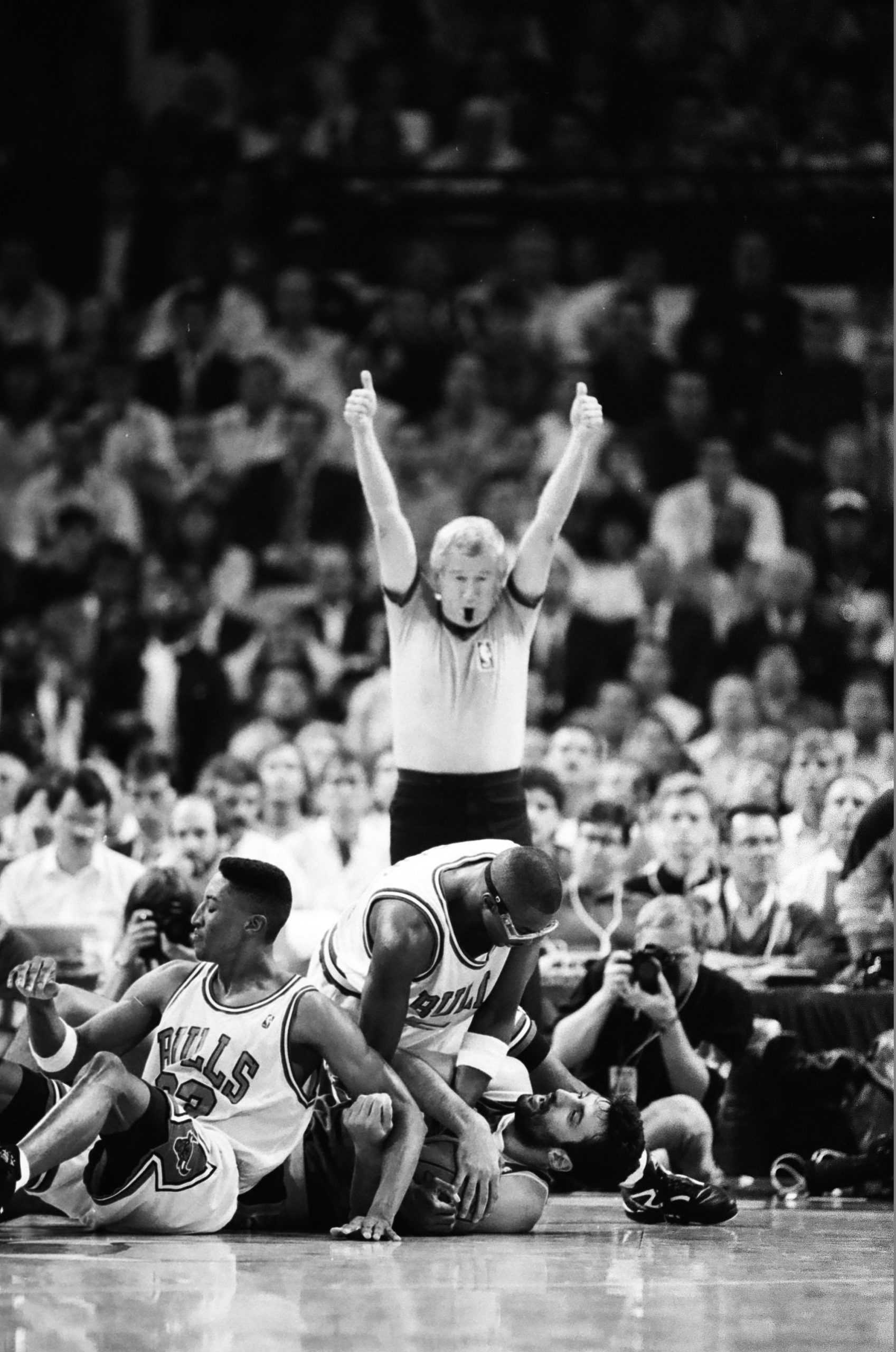 Referee signaling a jump ball with three players on the court