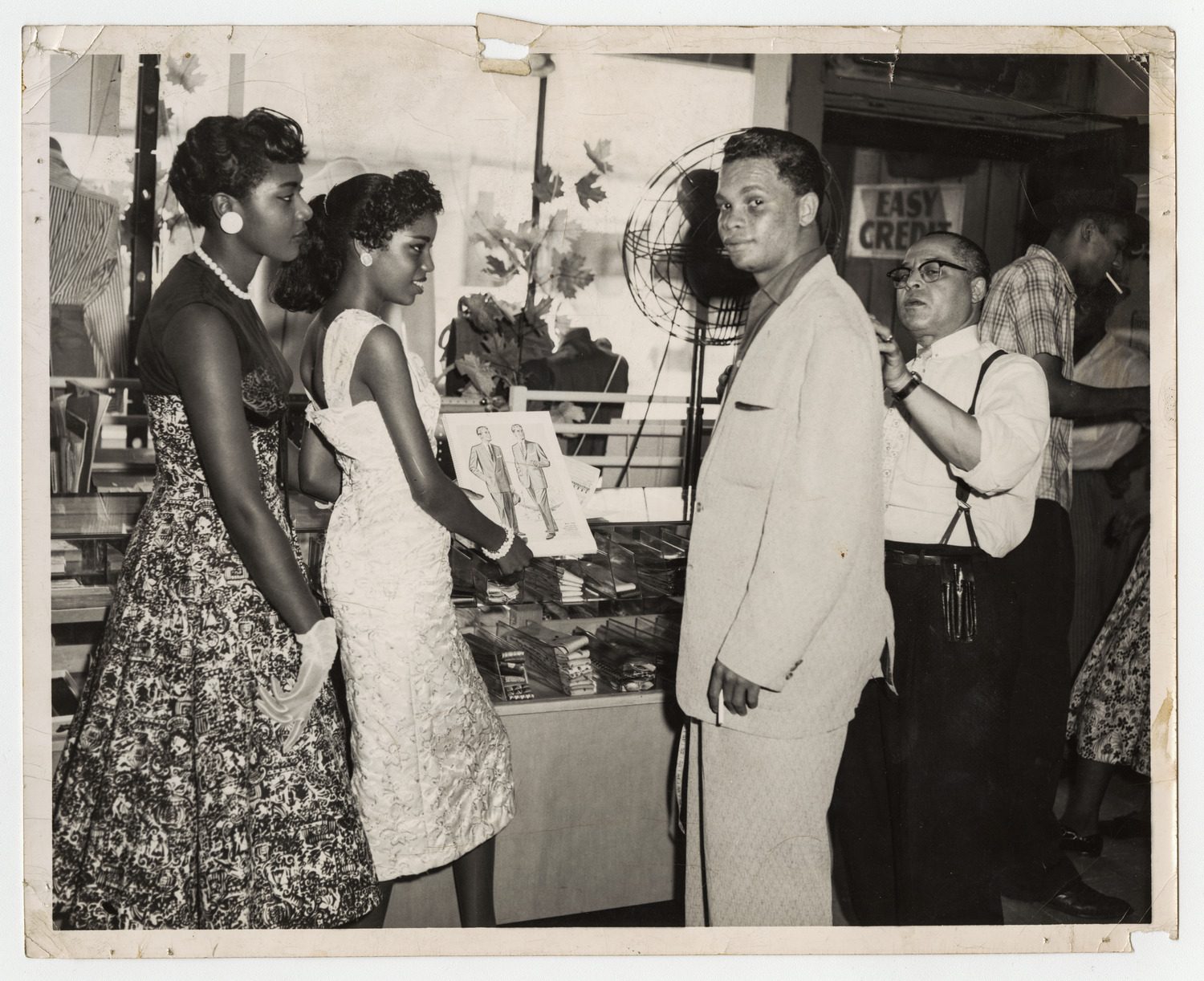 Man being measured for a suit in a clothing store as two women in dresses stand by, circa 1940s-1950s.