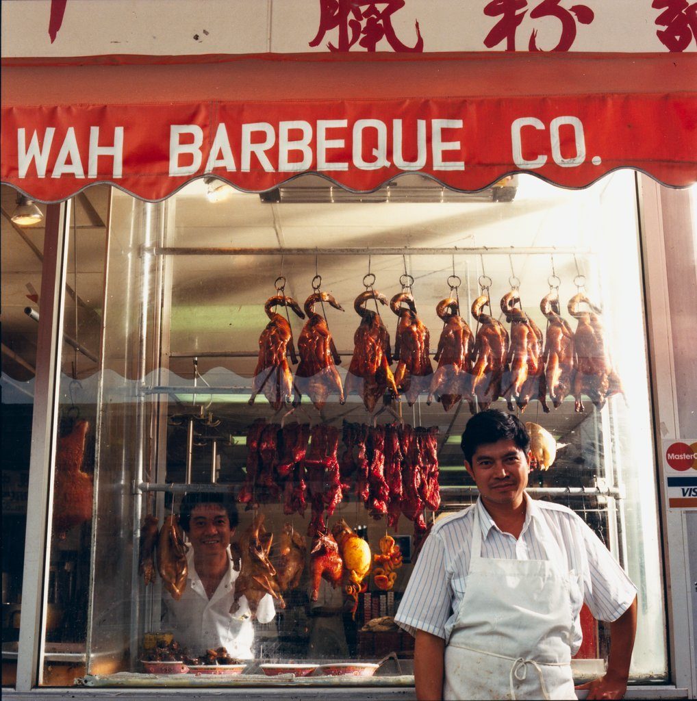 Owner, Eric Cheng, standing in front of Sun Wah Barbeque Company at 1134 West Argyle Street with barbequed ducks on display, Chicago, Illinois, 1987. Chef Choi Hau is seen through the window.