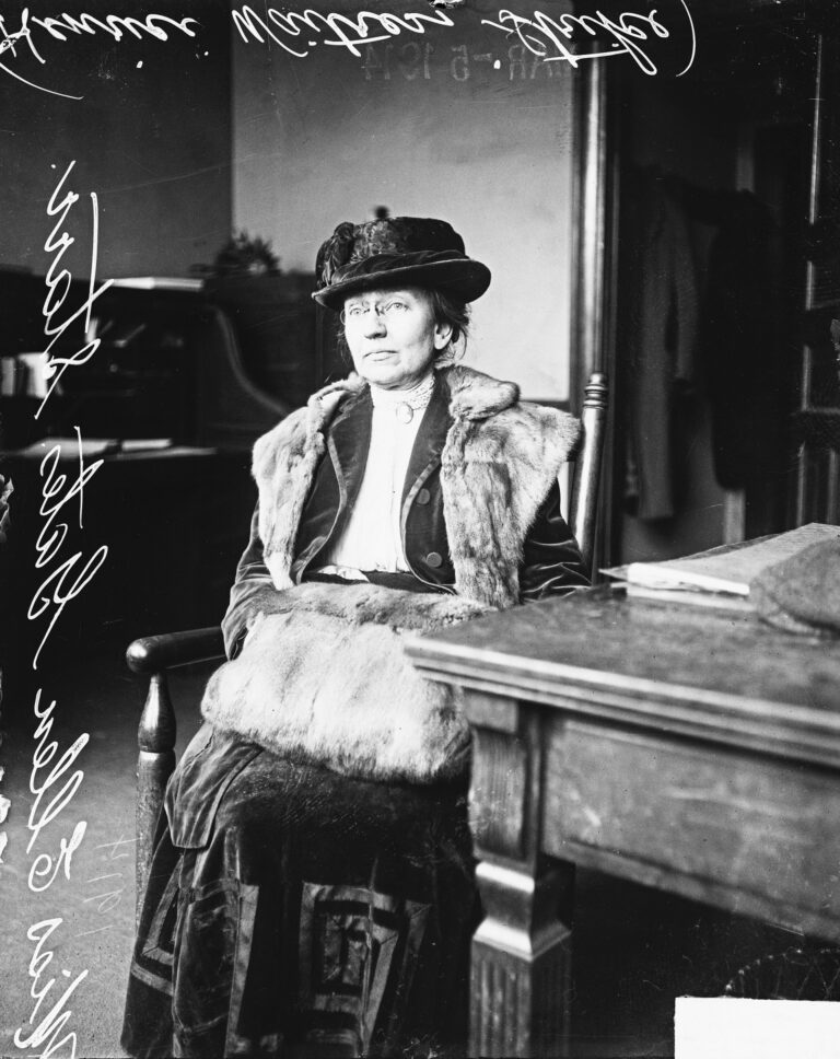Informal full-length portrait of Miss Ellen Gates Starr sitting next to a table in a room in Chicago